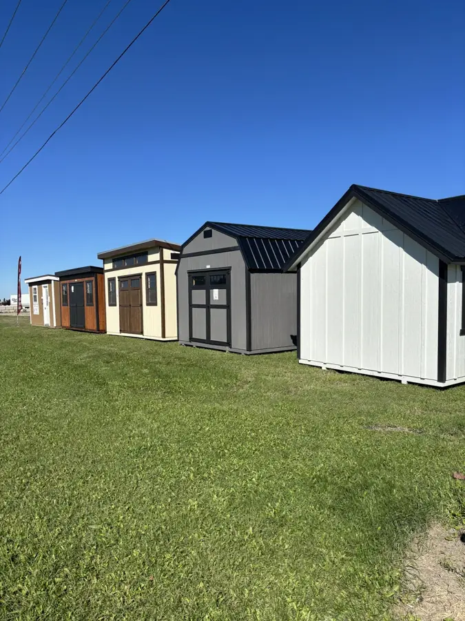 A row of Pine View sheds on display: a white classic shed, a grey lofted barn and modern sheds